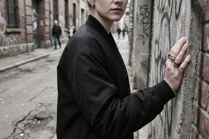 Jeune femme portant des bagues au style rebelle en argent oxydé appuyée contre un mur de béton urbain avec street art