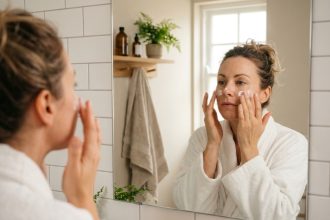 Femme prenant soin de sa peau devant un miroir de salle de bain, illustrant le lien entre routine beauté et confiance en soi